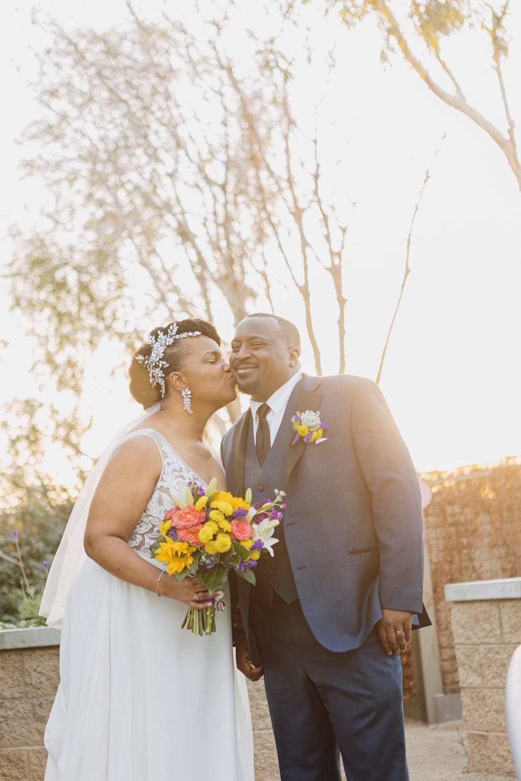 A bride kissing her groom's cheek at golden hour at Springs Preserve, a Scheme Events wedding