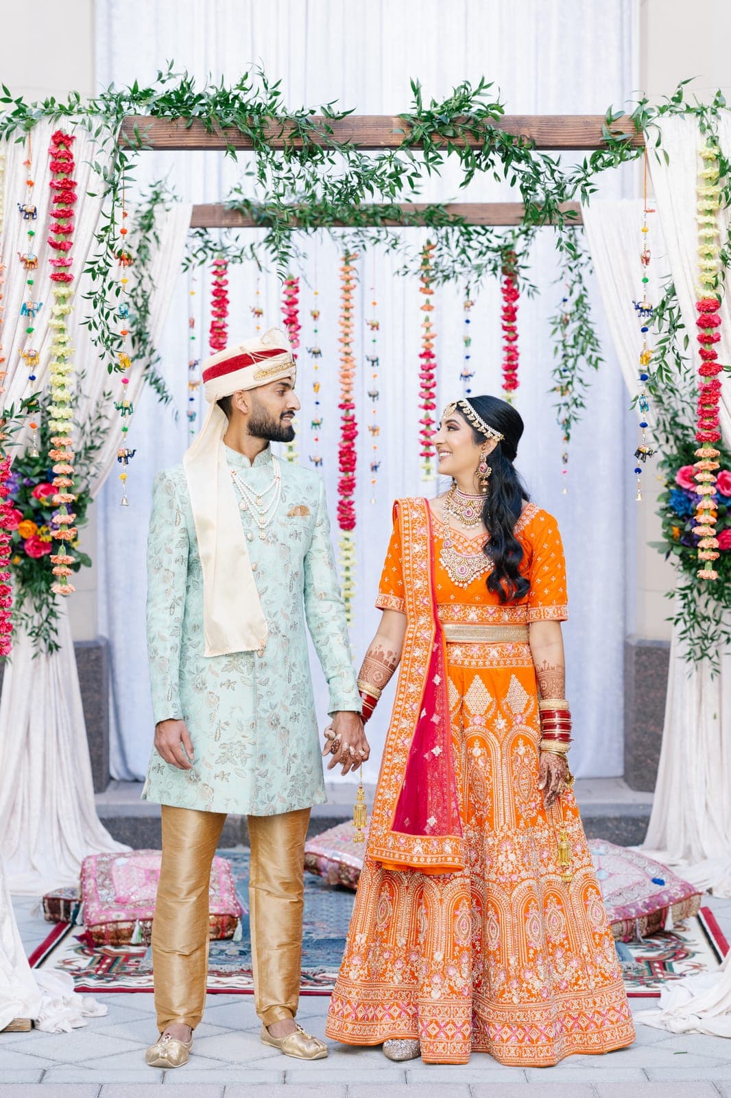 A bride in a vivid orange lehenga and her groom beneath a marigold-strung mandap at The Smith Center, a Scheme Events wedding