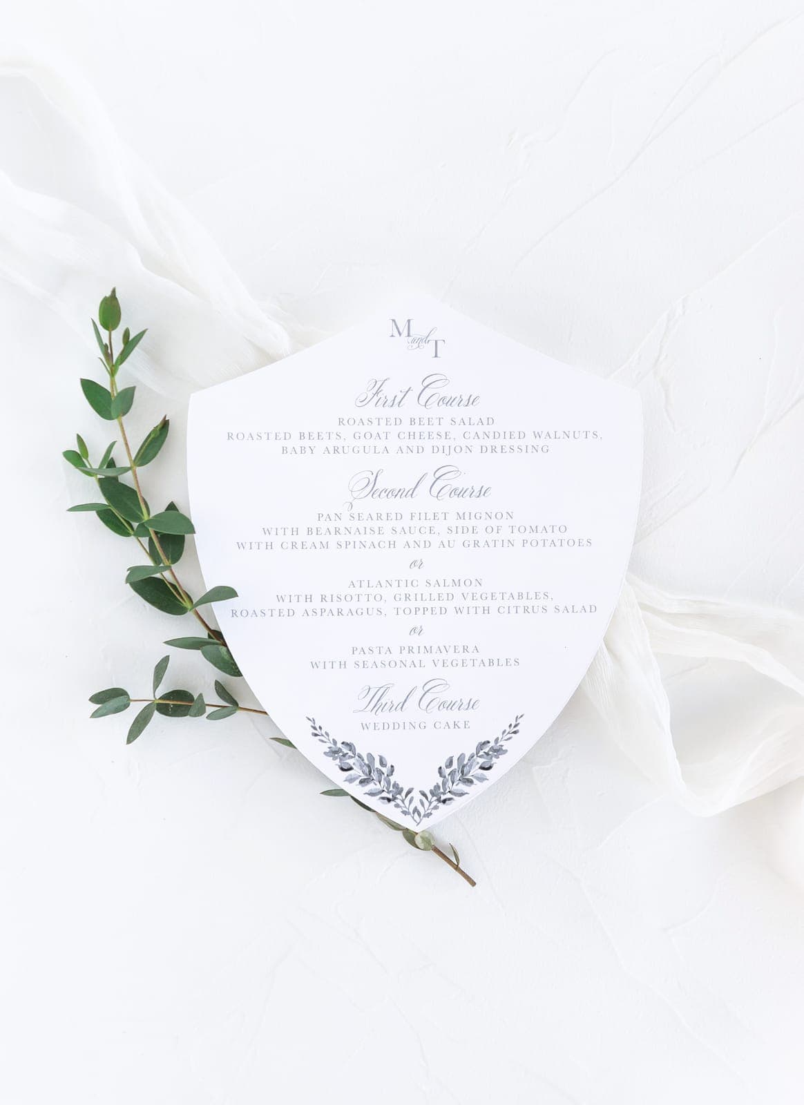A crest-shaped dinner menu with a eucalyptus sprig on silk, from a Scheme Events wedding at Southern Highlands